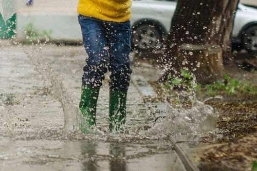Omanlainen äiti -blogin kuva, jossa henkilö pomppii vesilätäkössä kumpparit jalassa.
