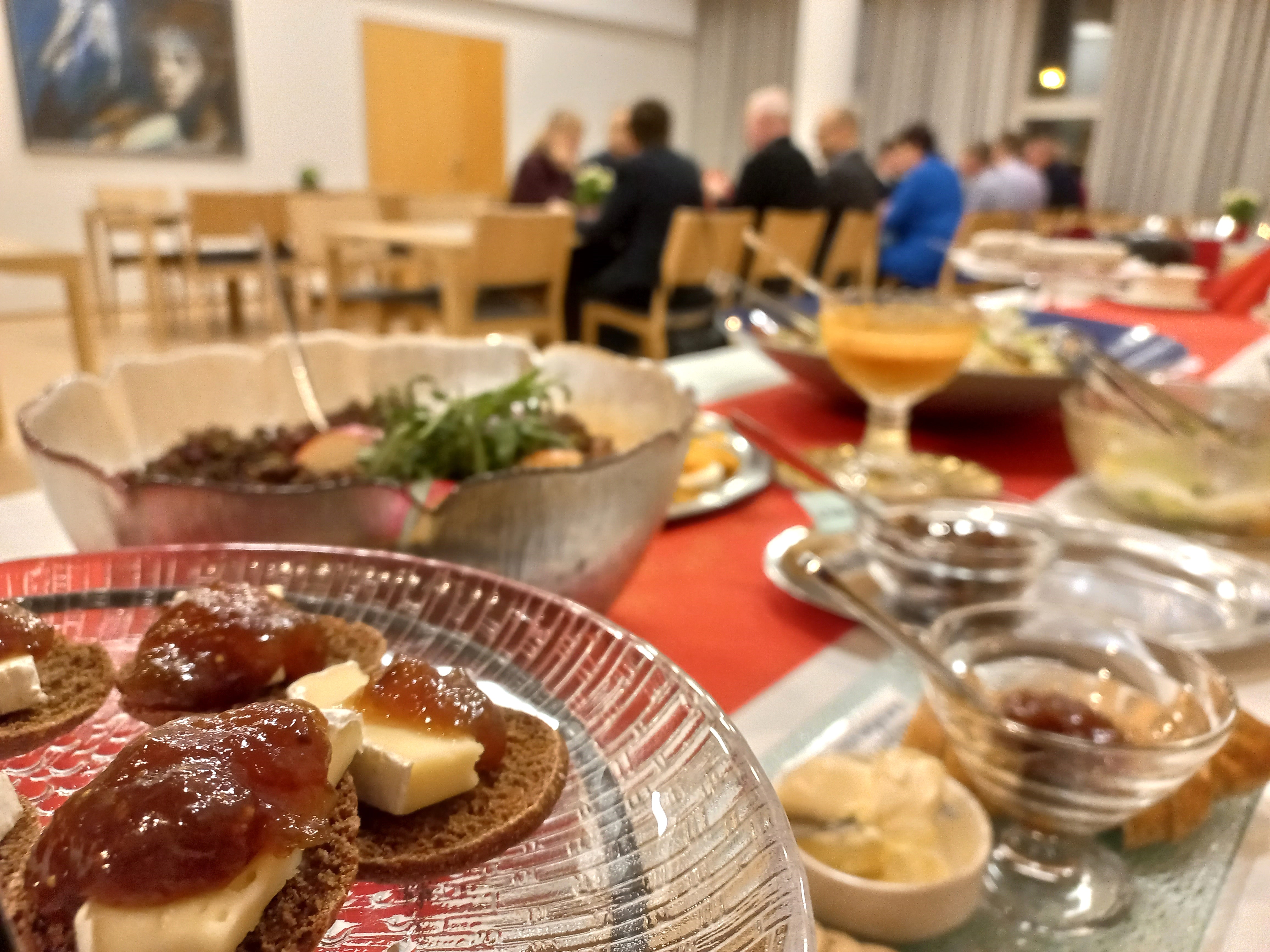 Pöytä täynnä astioita ja ruokaa. Taustalla ihmisiä.