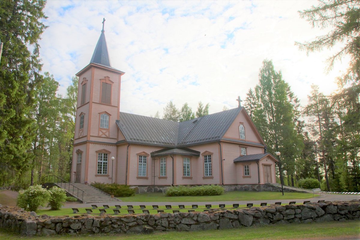 Anttolan puinen kirkko kesän vihreyden keskellä.