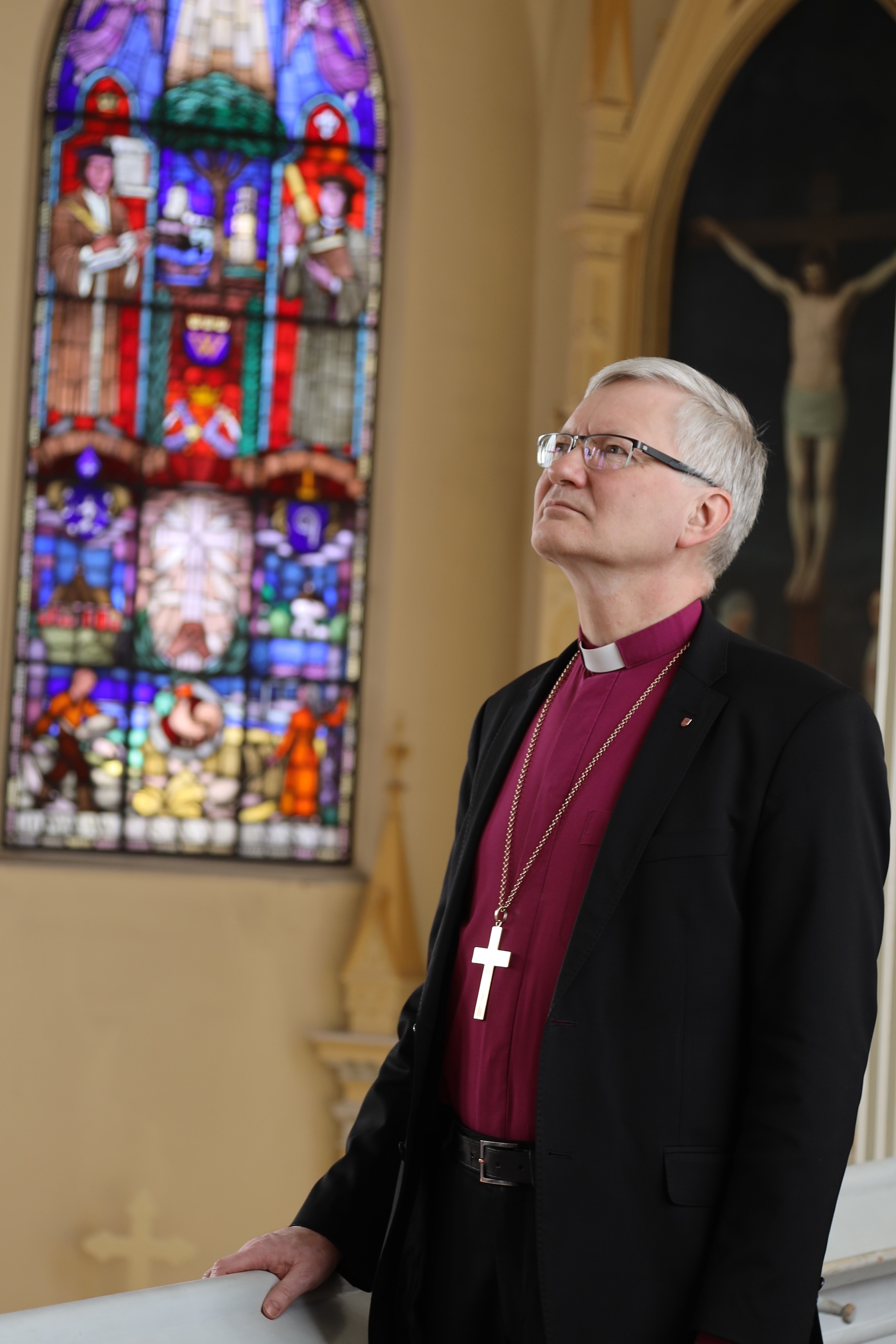 Piispa Seppo Häkkinen katsoo ylös valoon Mikkelin tuomiokirkon lehterillä. austalla näkyy 