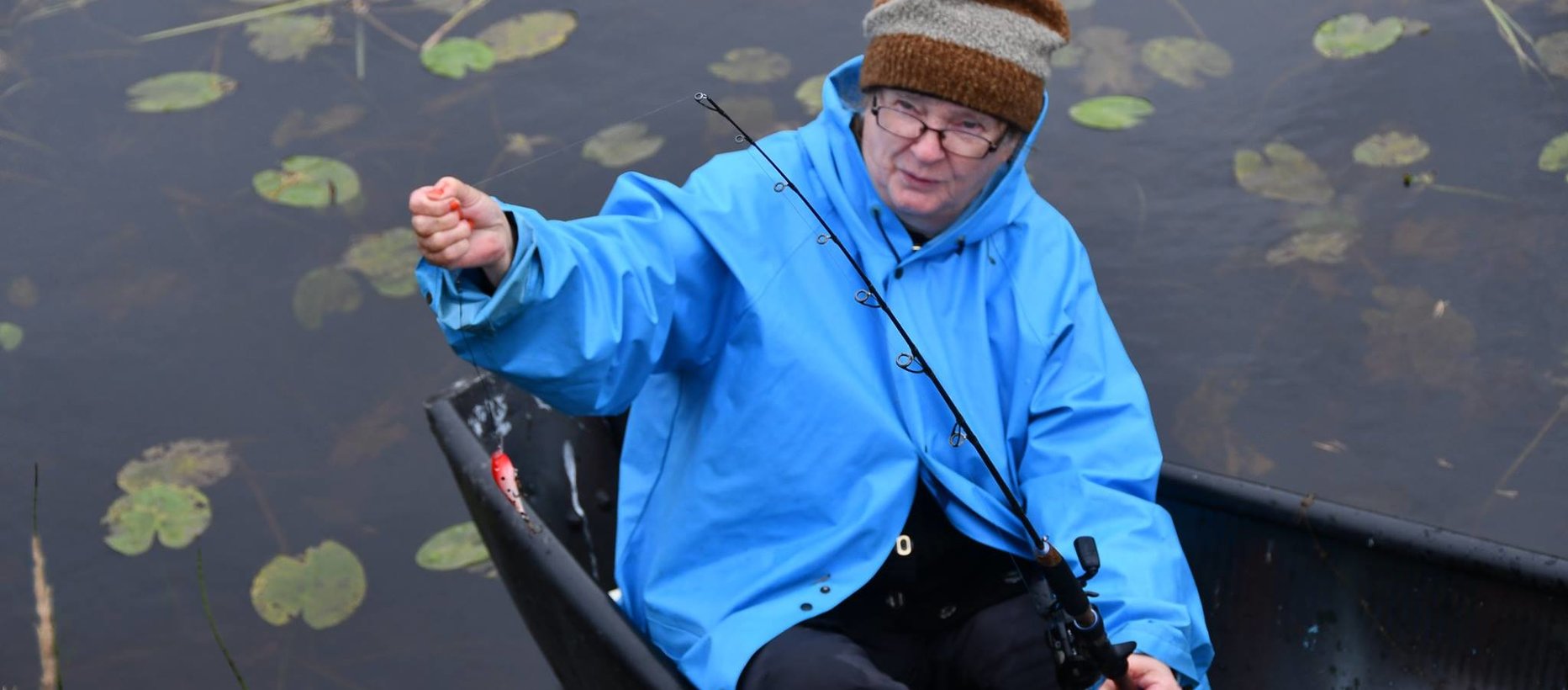 Liisa Heikkinen veneessä sininen sadetakki päällä kalassa.