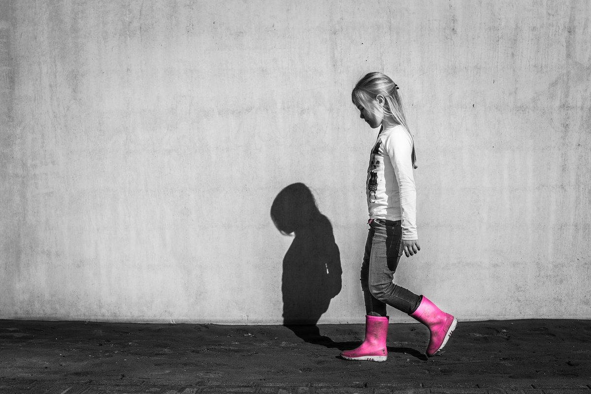 pieni tyttö kävelee pää painuksissa tyhjällä kadulla punaiset kumisaappaat jalassa