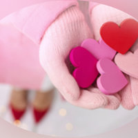 Nainen pitelee kasaa erivärisiä sydämiä käsissään, joissa vaaleanpunaiset sormikkaat.